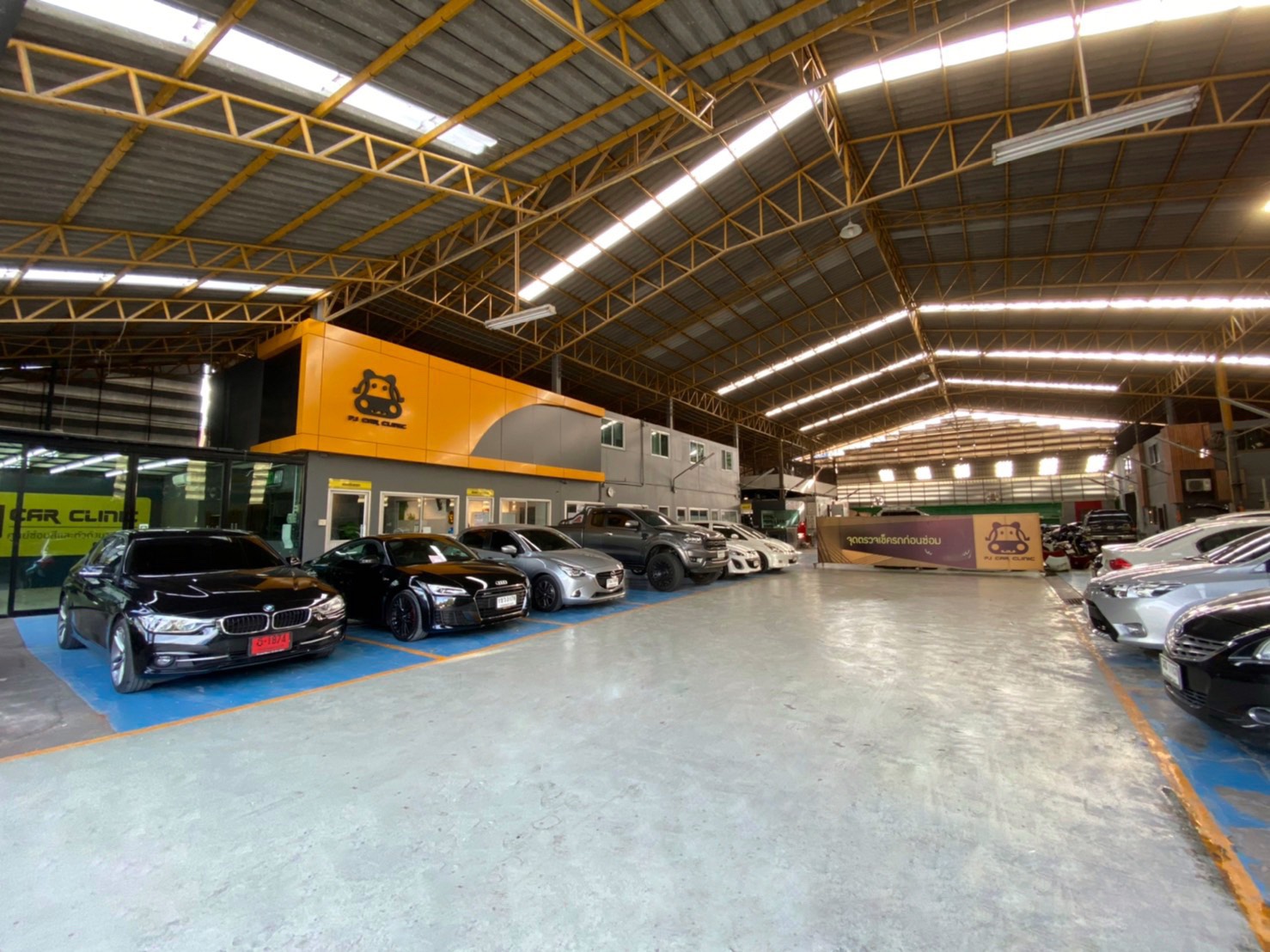 ภายในอู่ซ่อมรถ Car Clinic ที่มีรถยนต์หลายคันจอดอยู่ในโกดังขนาดใหญ่พร้อมสำนักงานสีเหลืองส้ม