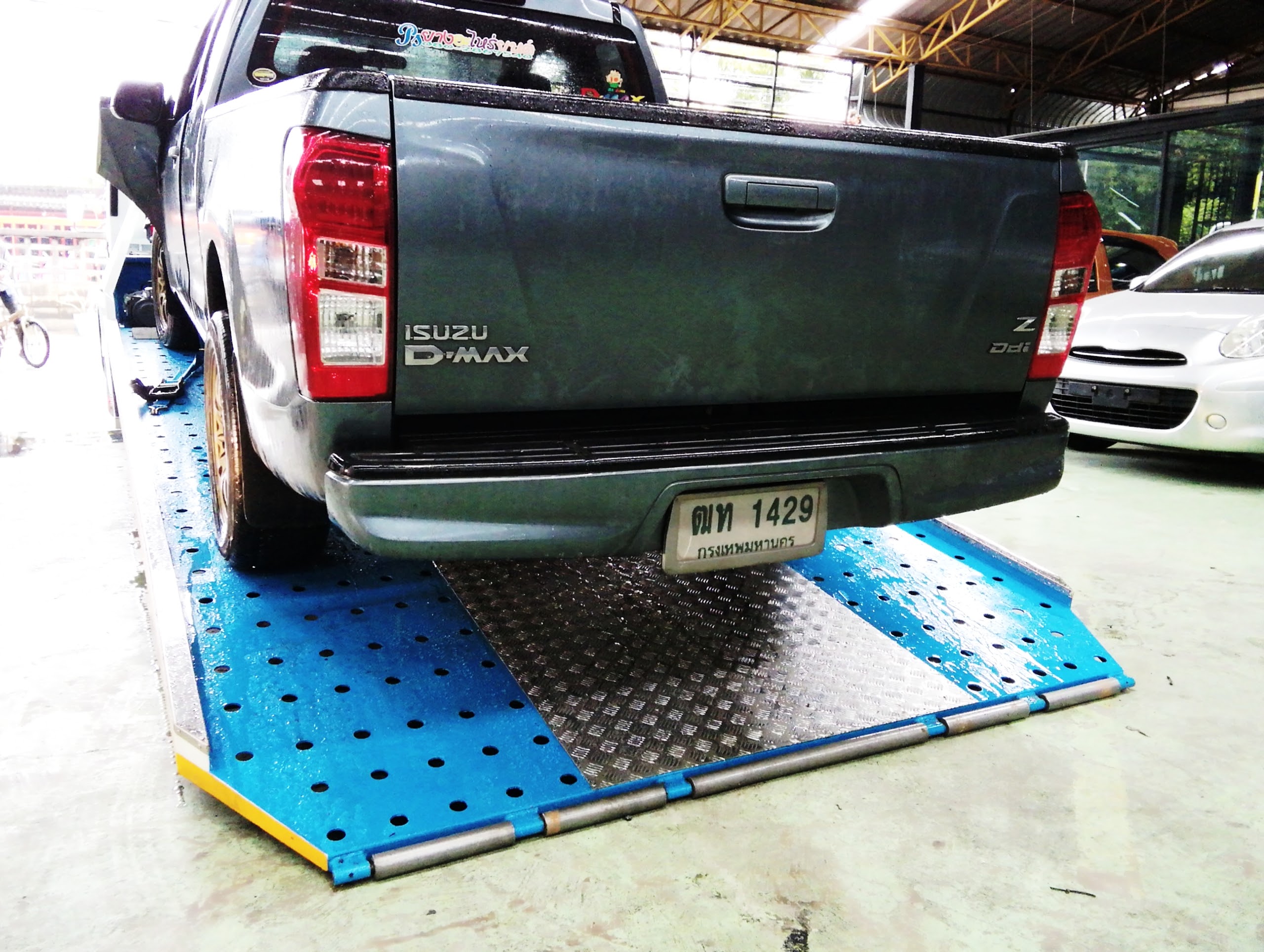 รถกระบะอีซูซุ ดีแมกซ์ สีเทาเข้ม จอดบนลิฟต์ยกรถสีฟ้าในอู่ซ่อมรถ