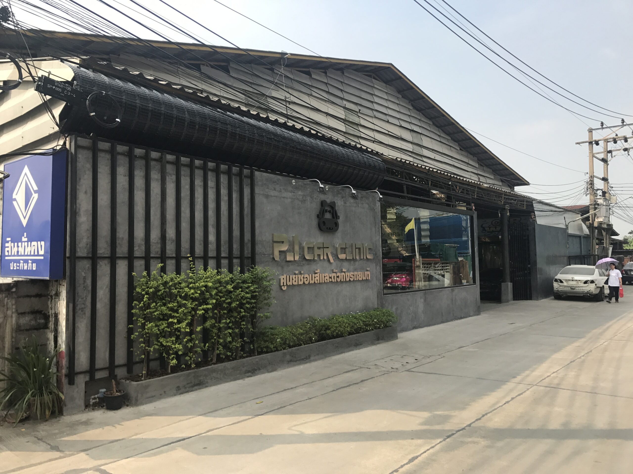 ด้านหน้าอาคาร PJ Car Clinic ศูนย์ซ่อมสีและตัวถังรถยนต์ มีป้ายสินมั่นคงประกันภัยอยู่ด้านข้าง