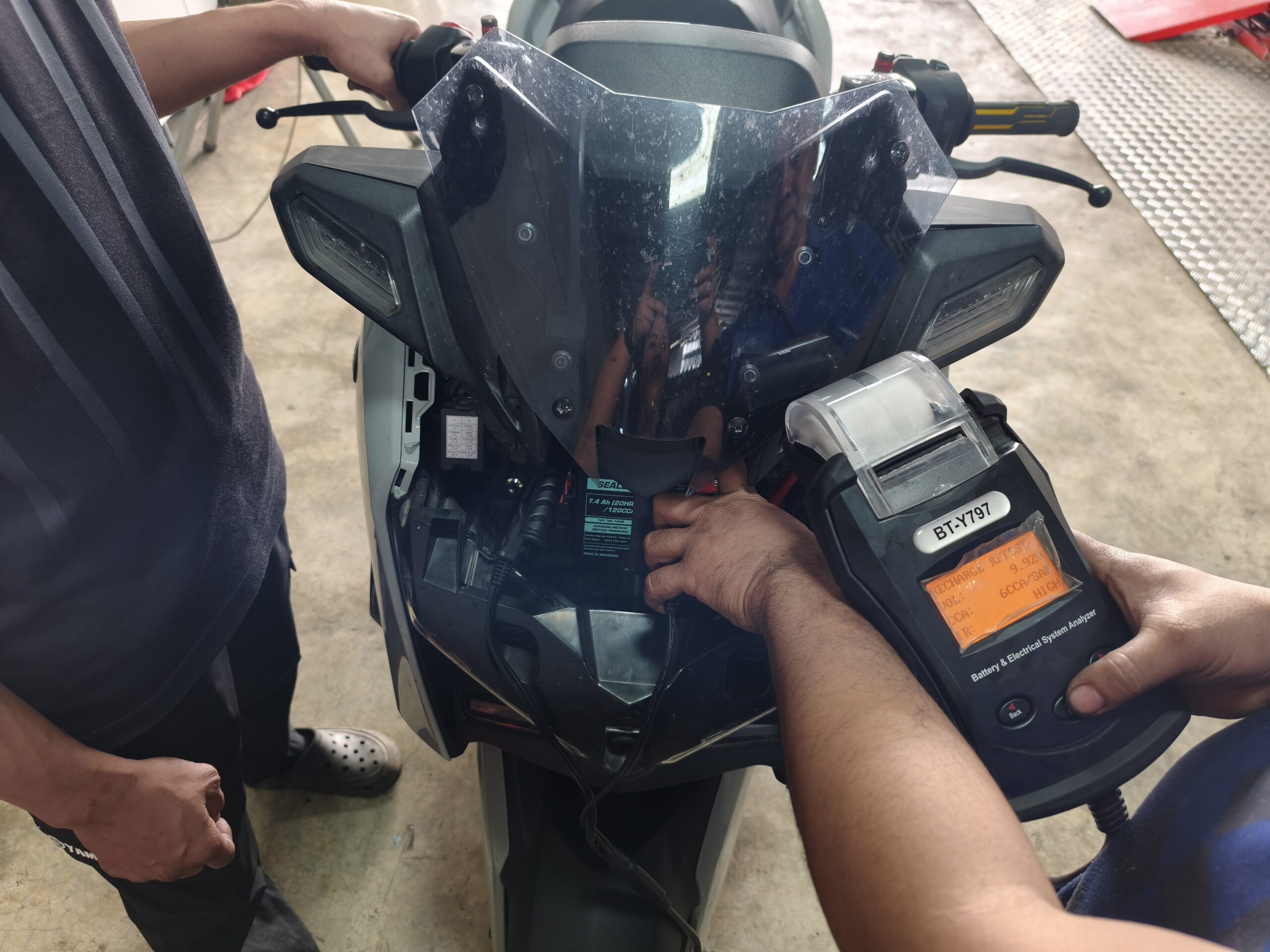 ช่างกำลังตรวจสอบระบบแบตเตอรี่และไฟฟ้าของรถมอเตอร์ไซค์ด้วยเครื่องวิเคราะห์แบตเตอรี่