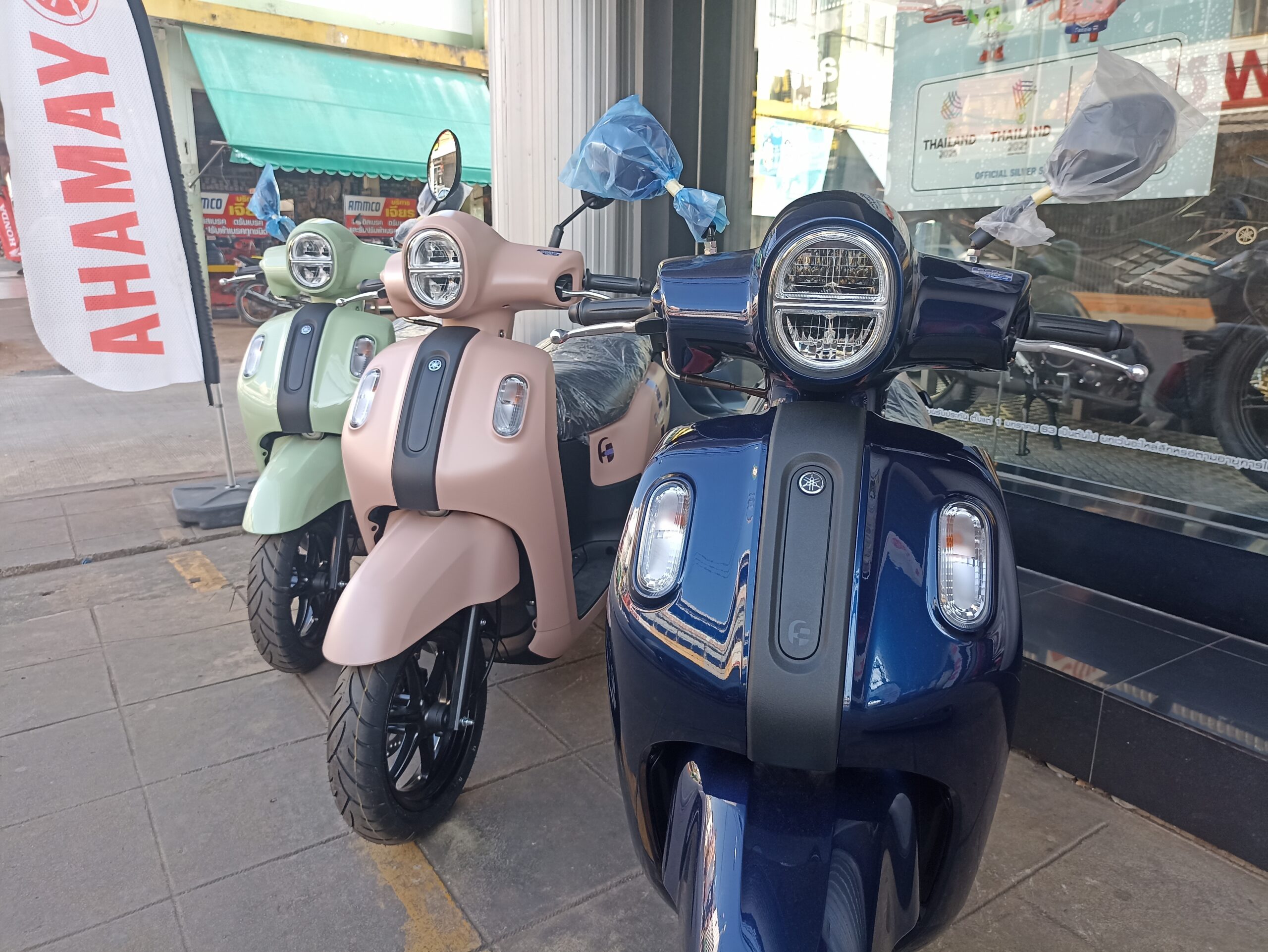 รถมอเตอร์ไซค์ยามาฮ่าสกู๊ตเตอร์หลายสีจอดโชว์หน้าร้านตัวแทนจำหน่ายในประเทศไทย สีน้ำเงิน ชมพู และเขียว
