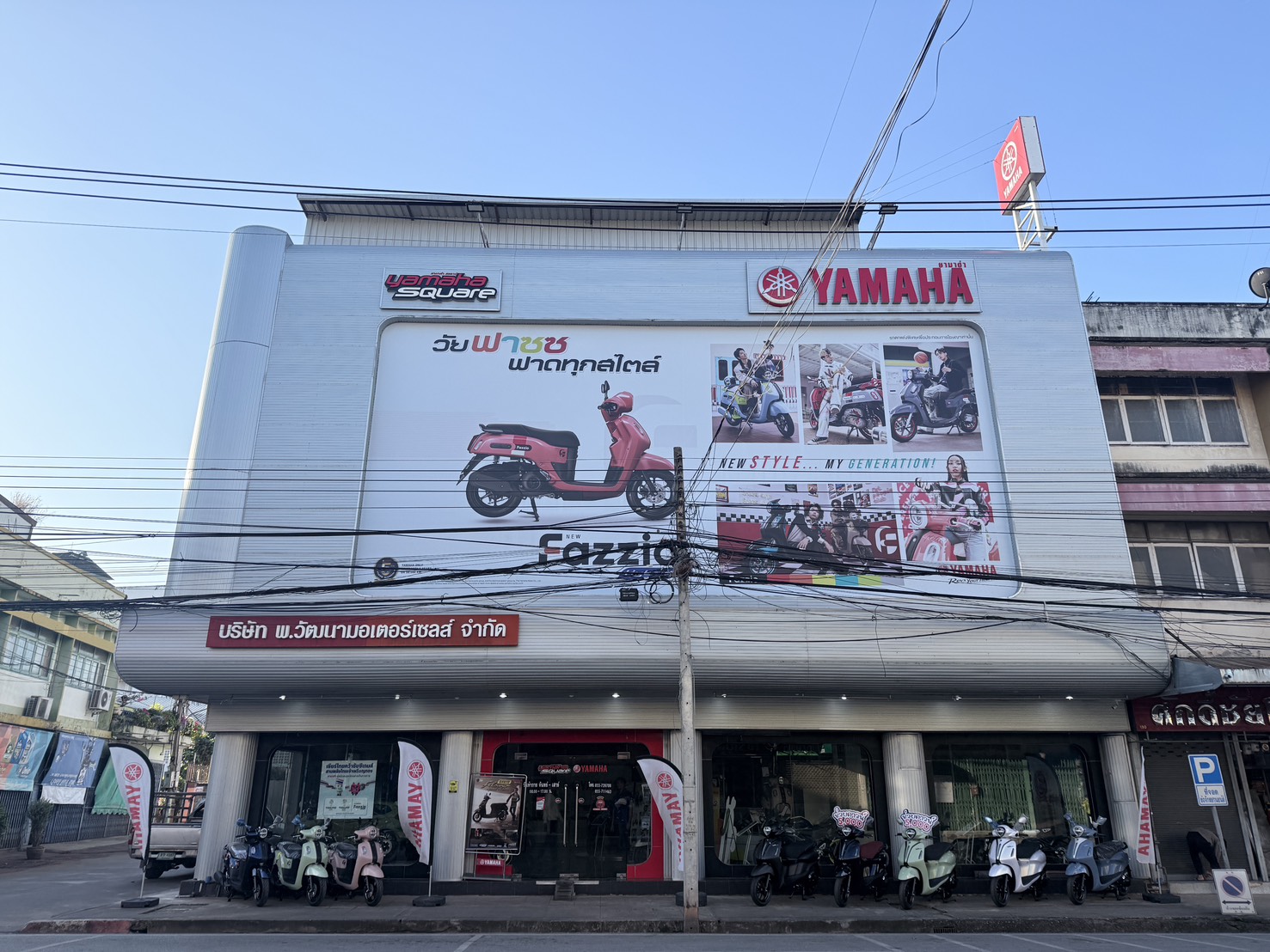 ร้านตัวแทนจำหน่ายรถจักรยานยนต์ยามาฮ่าสแควร์ พร้อมป้ายโฆษณารุ่น Fazzio สีชมพู และรถมอเตอร์ไซค์จอดหน้าร้าน