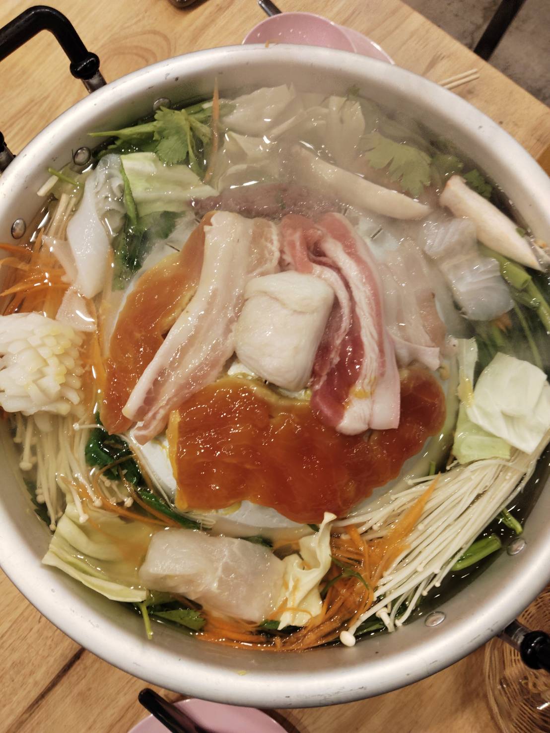 หม้อชาบูสุกี้ใส่เนื้อหมูสไลด์ เห็ดเข็มทอง ผักกาดขาว แครอท ผักชี และน้ำซุปใส บนโต๊ะไม้ในร้านอาหาร