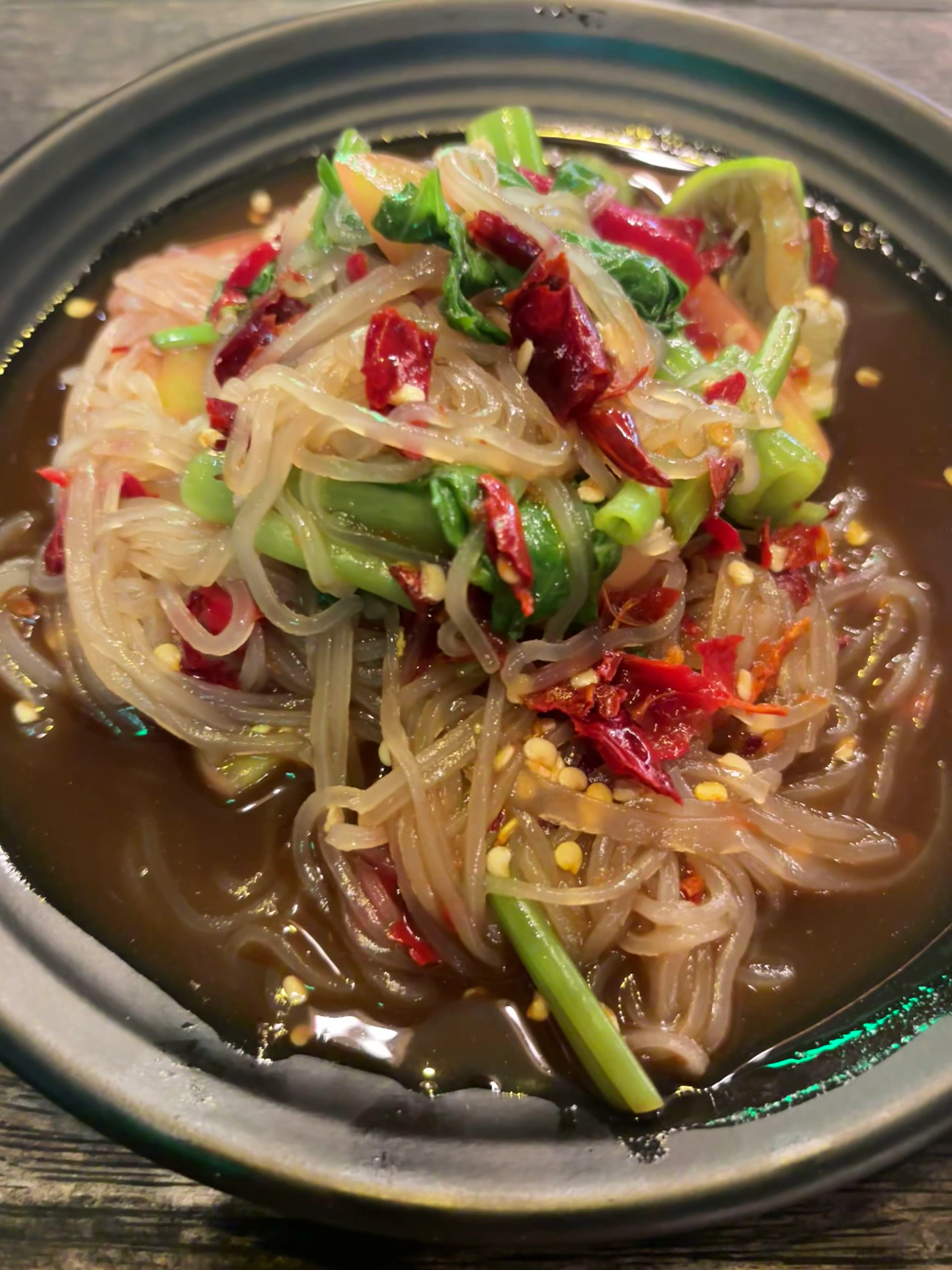 วุ้นเส้นผัดพริกแห้งในชามดำ มีผักบุ้งและพริกแห้งโรยหน้า น้ำซุปรสจัด