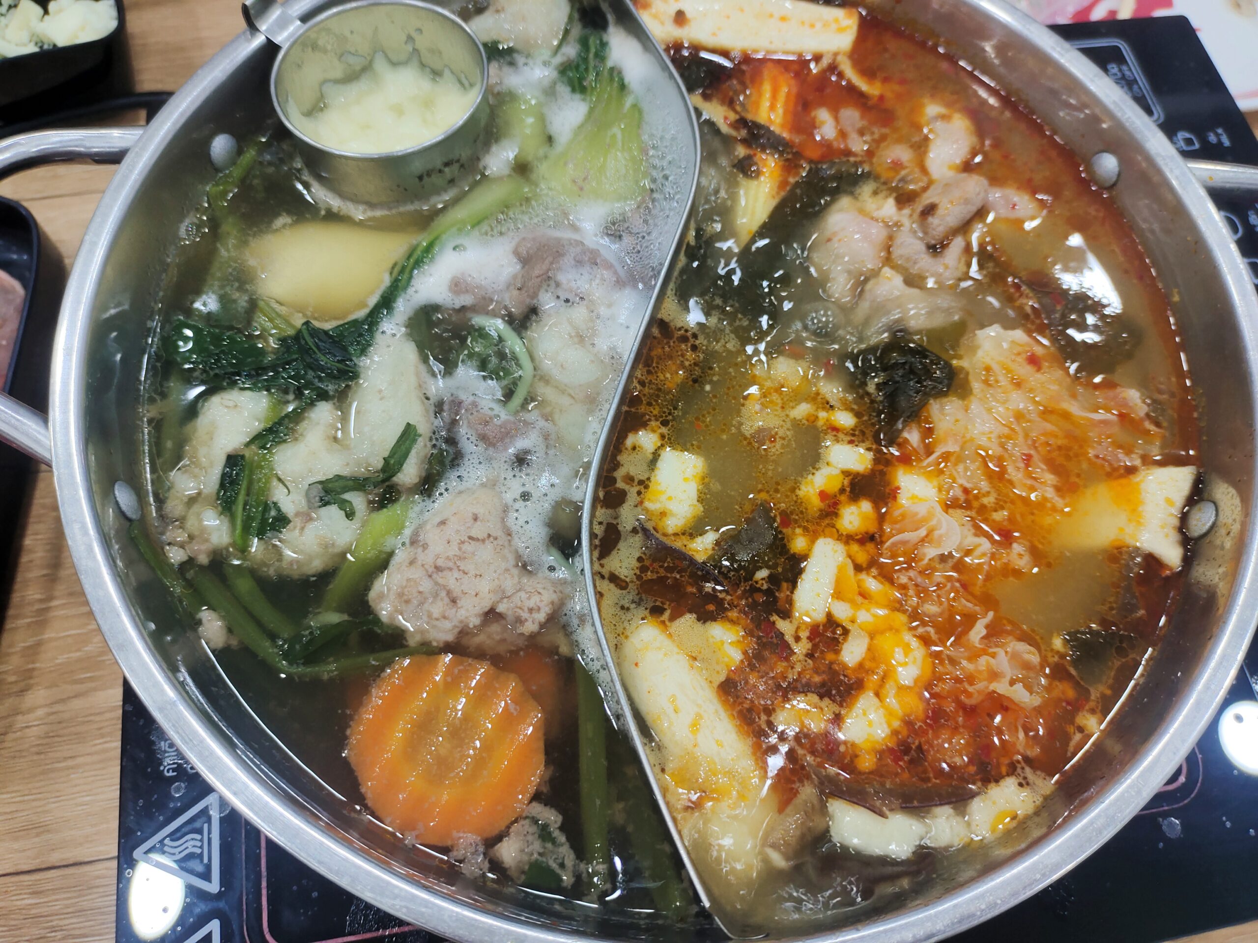 หม้อไฟชาบูสองช่อง แบ่งเป็นน้ำซุปใสใส่ผักและลูกชิ้น กับน้ำซุปรสเผ็ดใส่เต้าหู้และเนื้อสัตว์