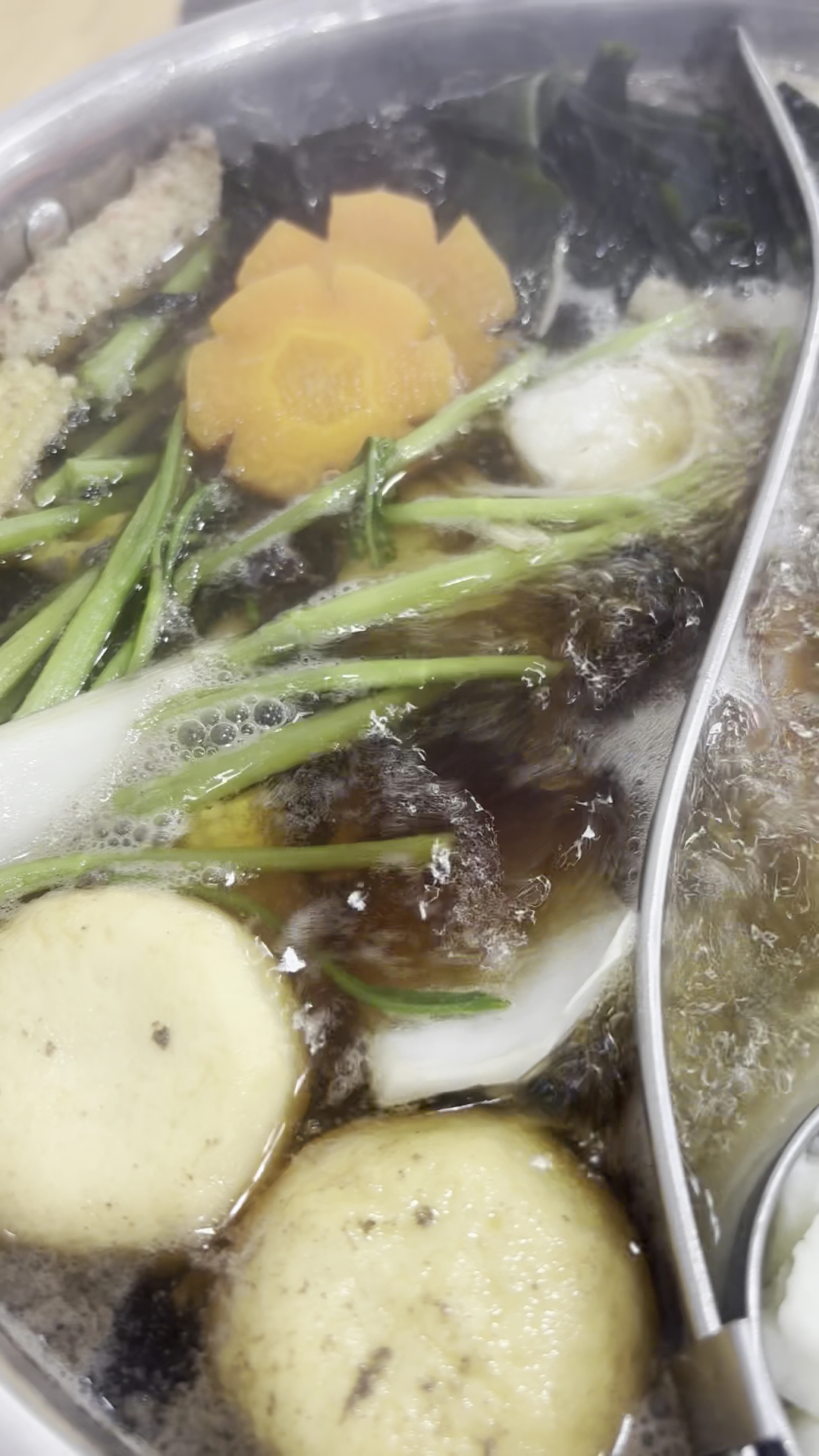 หม้อต้มน้ำซุปร้อนใส่ผักหลากชนิด มีมันฝรั่ง แครอทแกะสลักดอกไม้ ต้นหอม สาหร่าย และเส้น กำลังเดือดในหม้อสแตนเลส