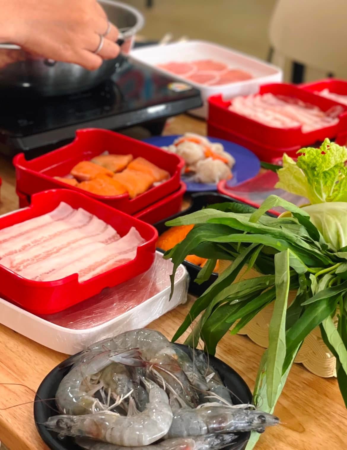 วัตถุดิบชาบูหม้อไฟ มีกุ้งสด เนื้อหมูสไลด์ แซลมอน ผักบุ้ง และผักสดบนโต๊ะไม้