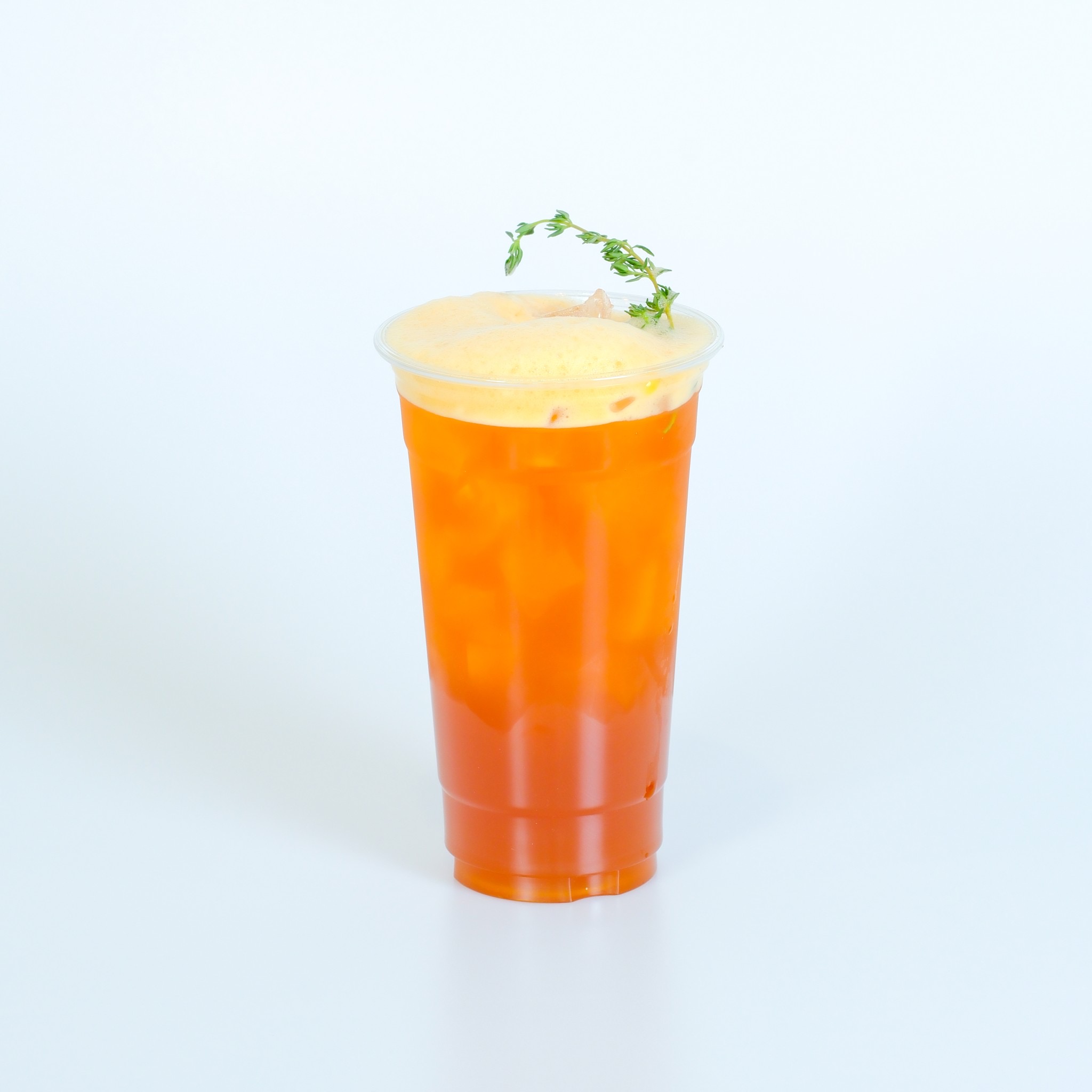 ชาเย็นสีส้มในแก้วพลาสติกใส ท็อปด้วยโฟมครีมชีสและตกแต่งด้วยใบไทม์สด