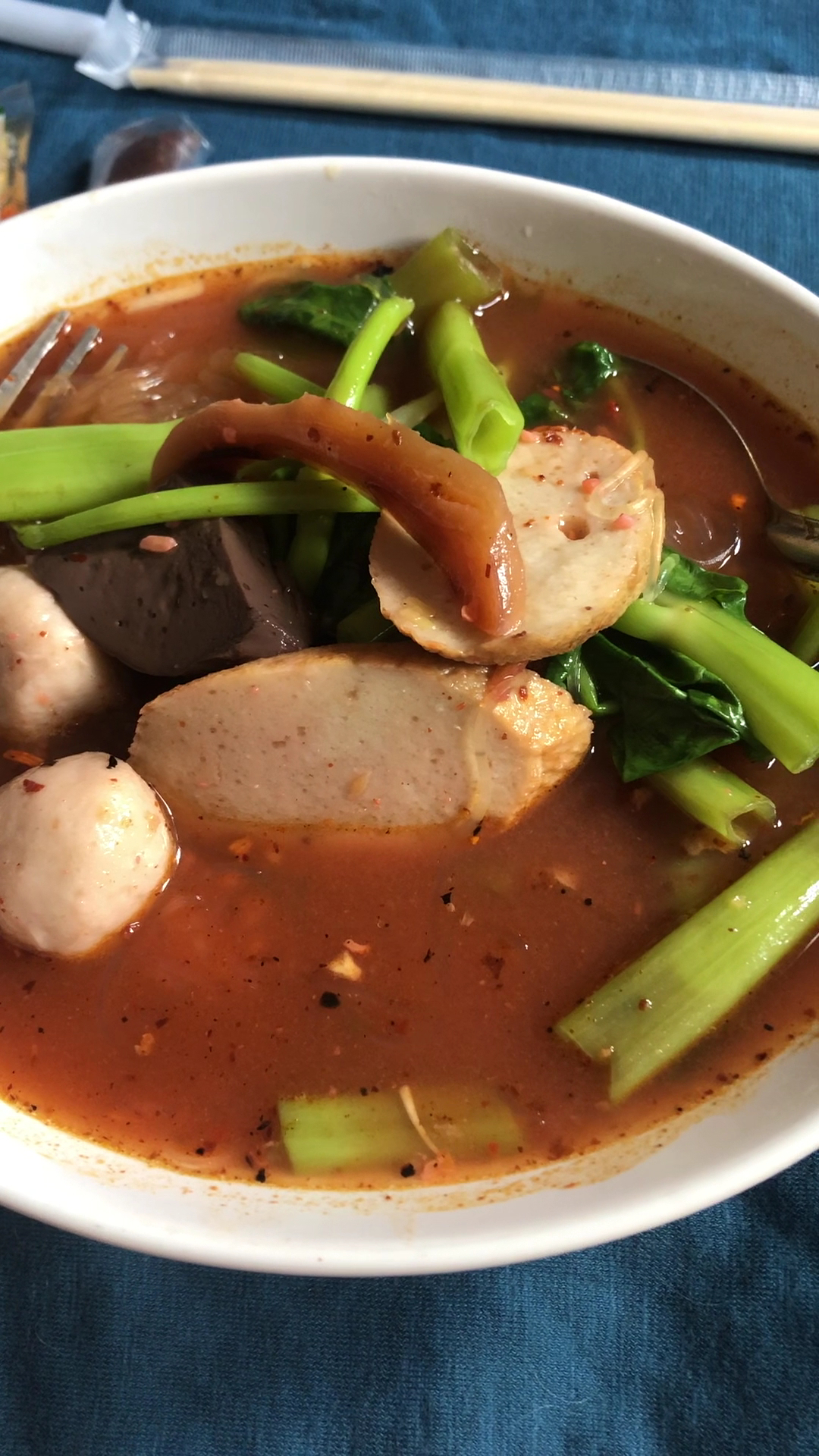 ก๋วยเตี๋ยวเรือน้ำตกใส่ลูกชิ้น หมูสไลซ์ ผักคะน้า และเครื่องในในชามสีขาว