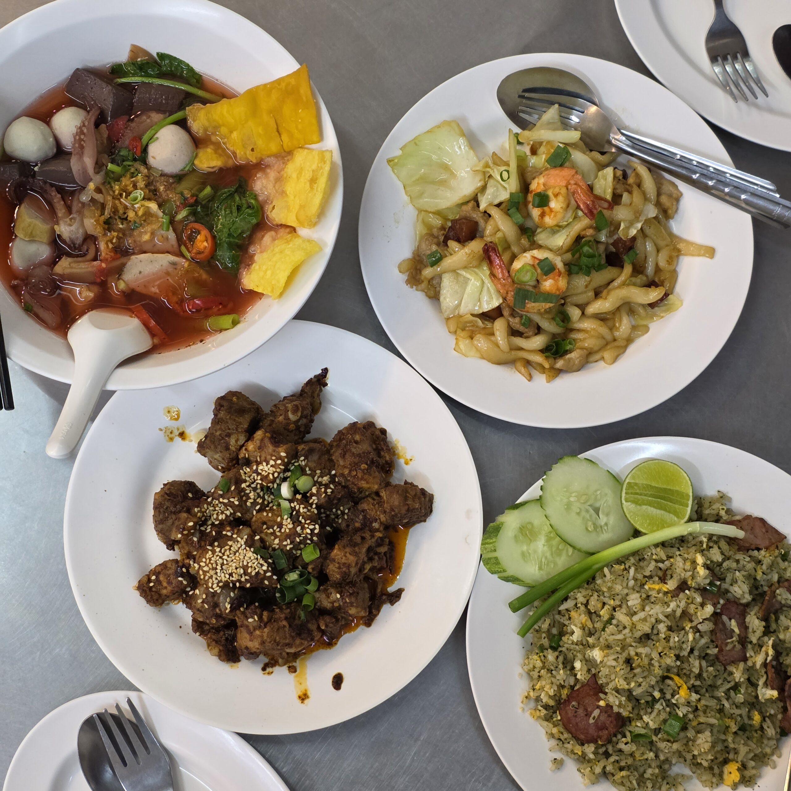 อาหารไทยหลายจาน บนโต๊ะมีเย็นตาโฟทะเล ผัดอุด้งกุ้ง ไก่ทอดซอสงาขาว และข้าวผัดกุนเชียงเสิร์ฟพร้อมแตงกวาและมะนาว