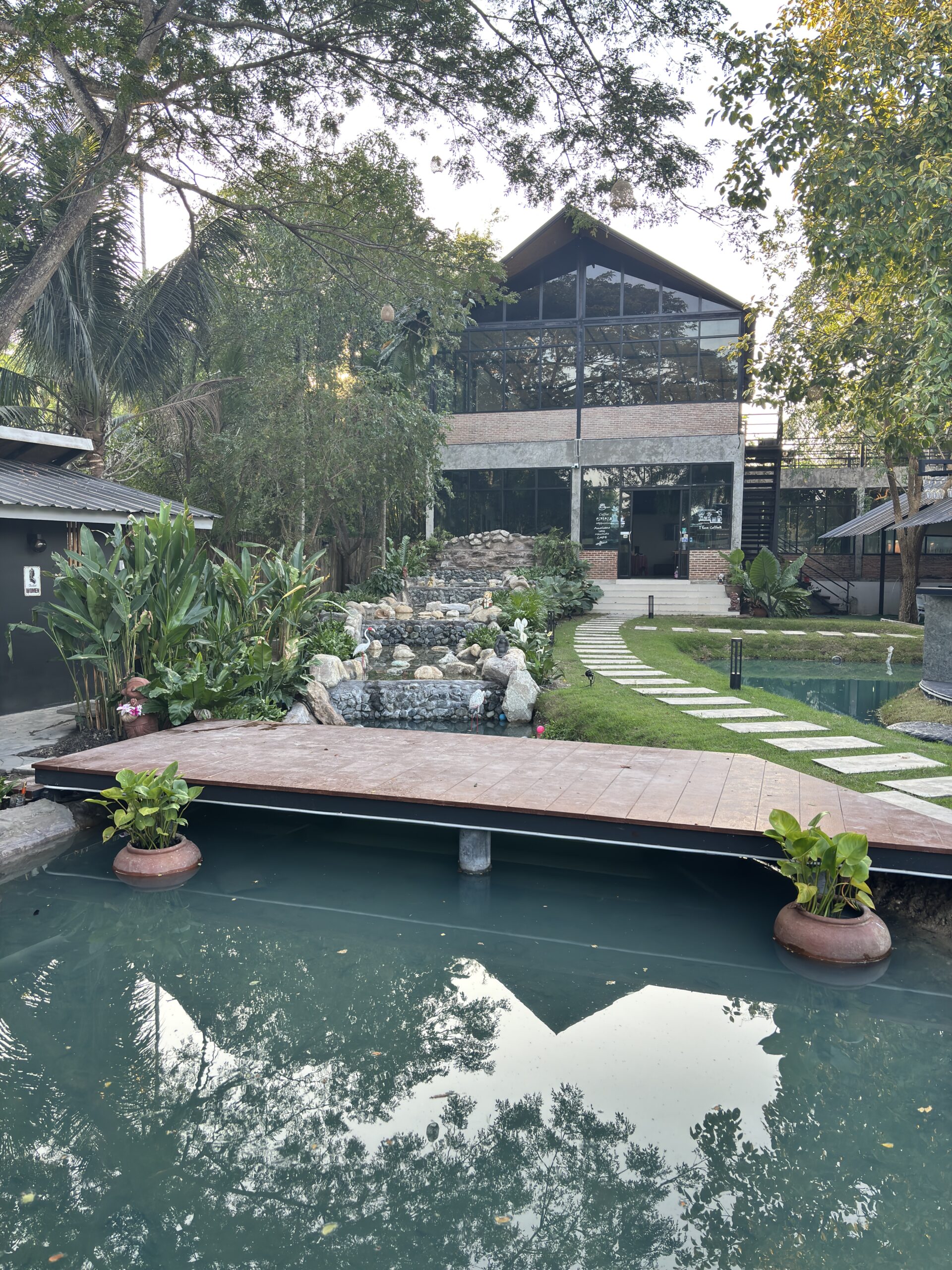 ร้านอาหารสไตล์โมเดิร์นลอฟท์กระจกใหญ่ มีสระน้ำ น้ำตกหินจำลอง สะพานไม้ และสวนสีเขียวร่มรื่น