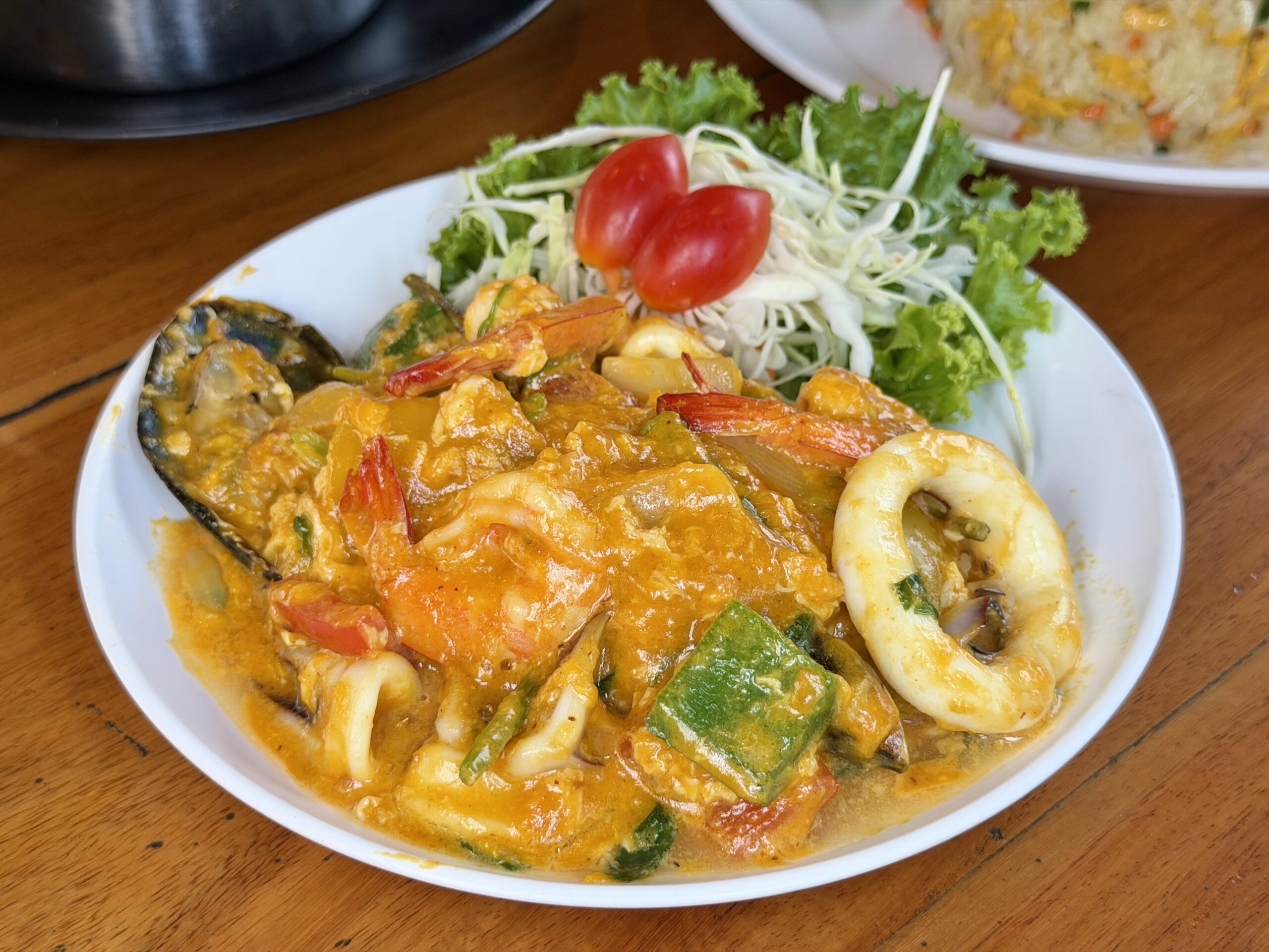 จานอาหารทะเลผัดผงกะหรี่รวมมิตร มีกุ้ง หมึก หอยแมลงภู่ พริก และผักในซอสกะหรี่สีเหลืองทอง เสิร์ฟพร้อมผักสลัดและมะเขือเทศราชินี