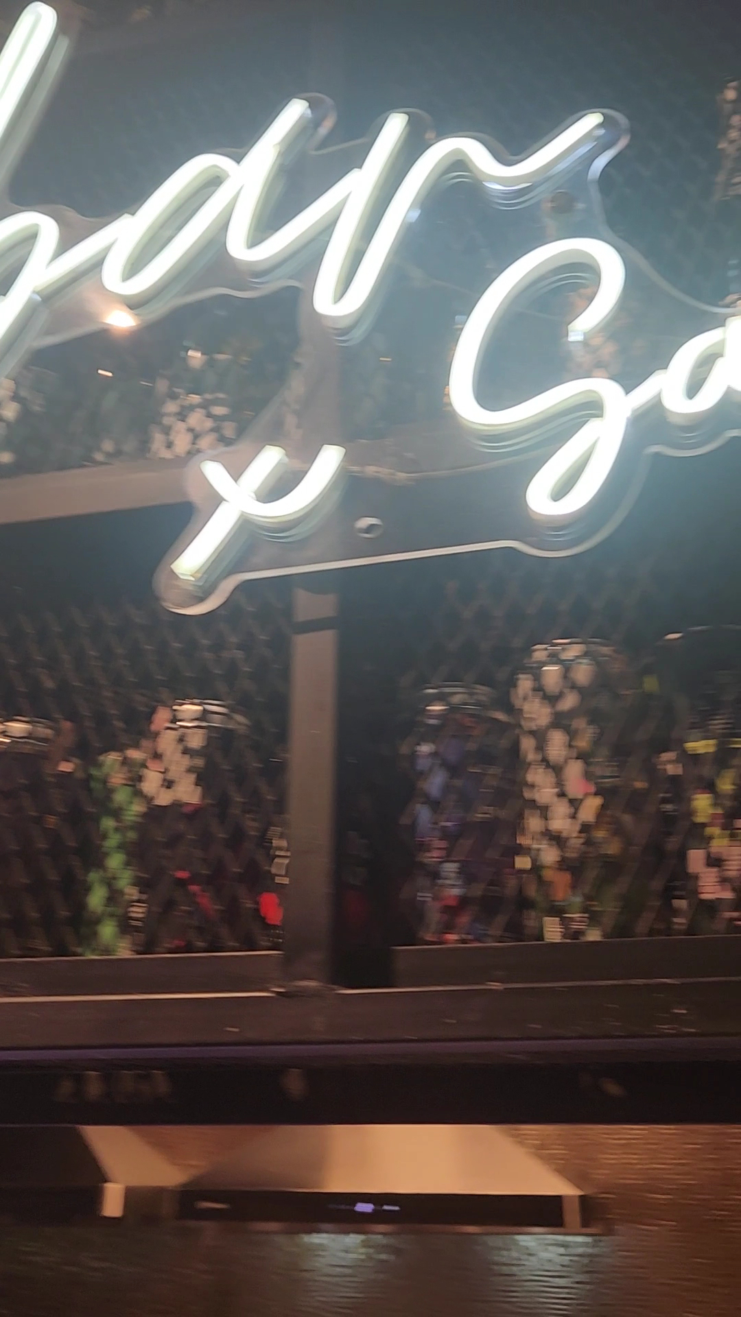 ป้ายไฟนีออนตัวอักษรสีขาวสไตล์เขียนมือภายในร้านอาหารบรรยากาศมืดพร้อมดอกไม้ตกแต่งด้านหลัง