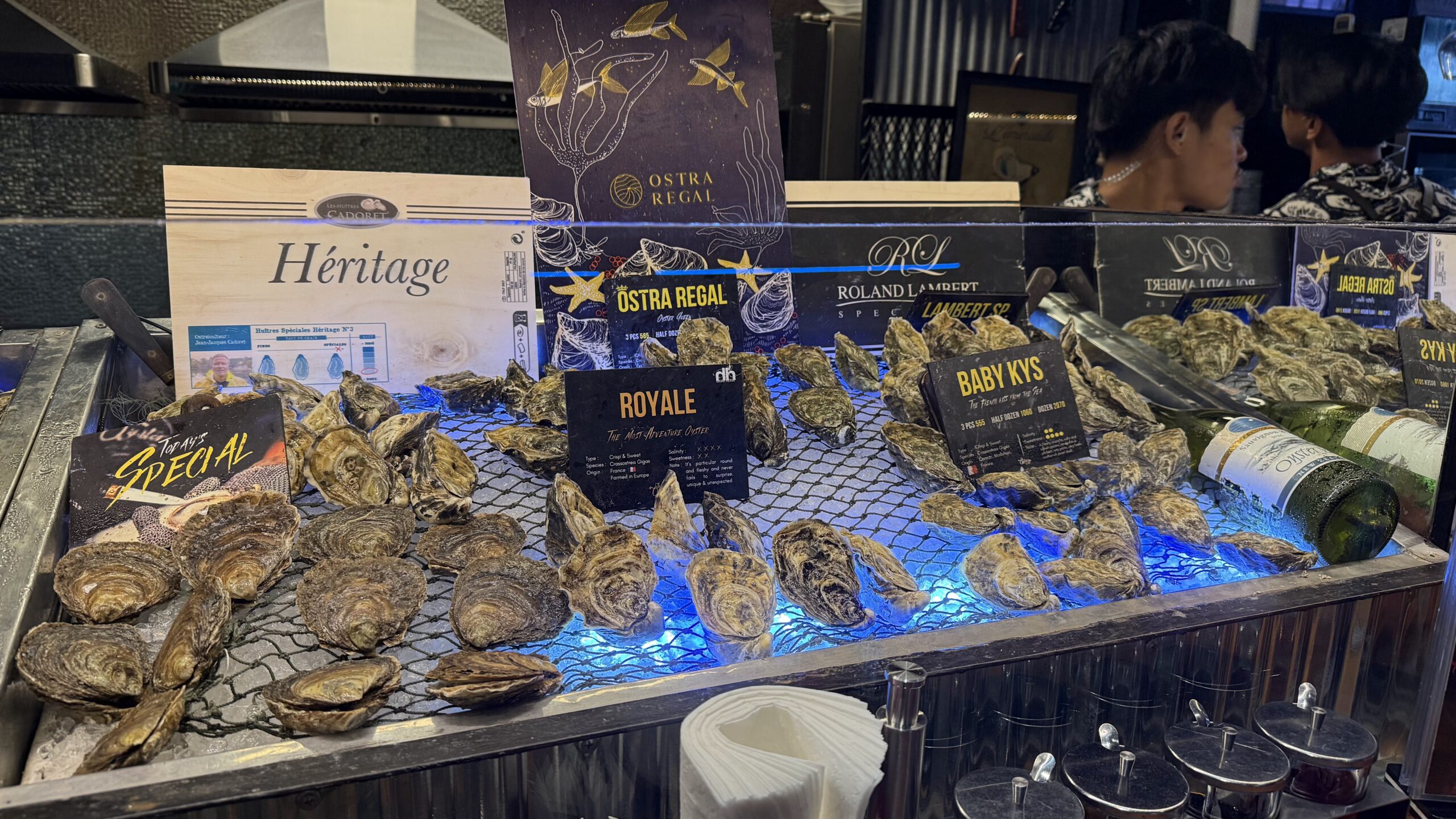 บาร์หอยนางรมสดพร้อมป้ายแบรนด์ Ostra Regal, Roland Lambert และ Héritage จัดแสดงบนน้ำแข็งพร้อมไฟสีน้ำเงิน