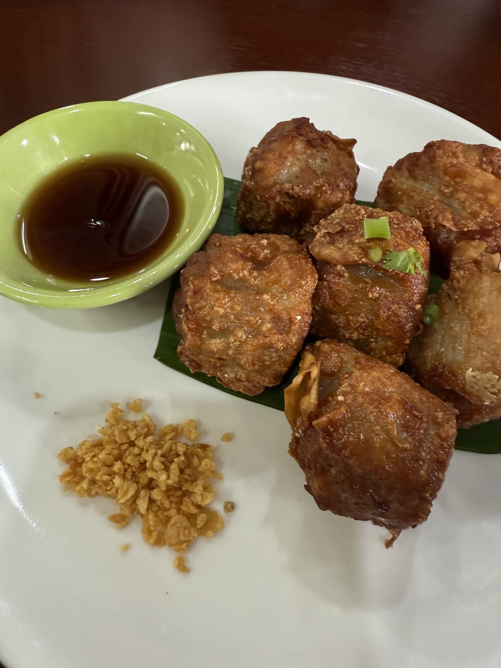 หมูทอดห่อแผ่นเต้าหู้ทอดกรอบเสิร์ฟพร้อมซอสเปรี้ยวหวานและกระเทียมเจียวบนจานขาว