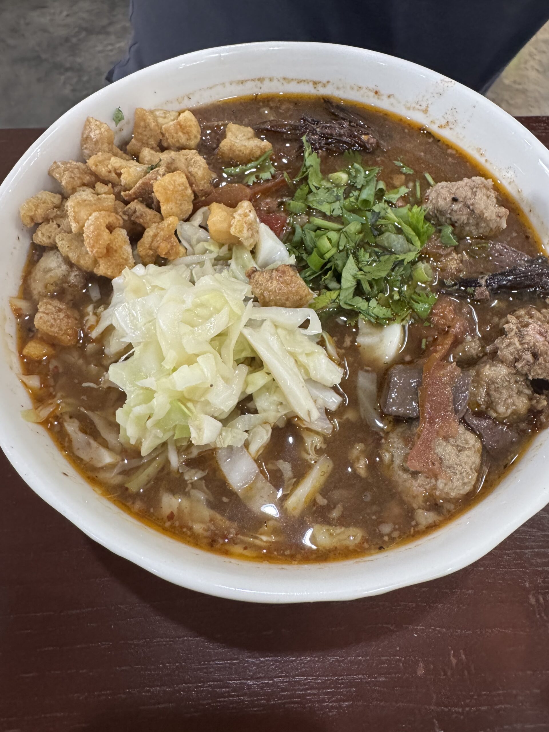 ก๋วยเตี๋ยวน้ำเงี้ยวในชามสีขาว พร้อมเนื้อหมู ผักกาดดอง แคบหมู ผักชี และน้ำซุปสีน้ำตาลเข้ม