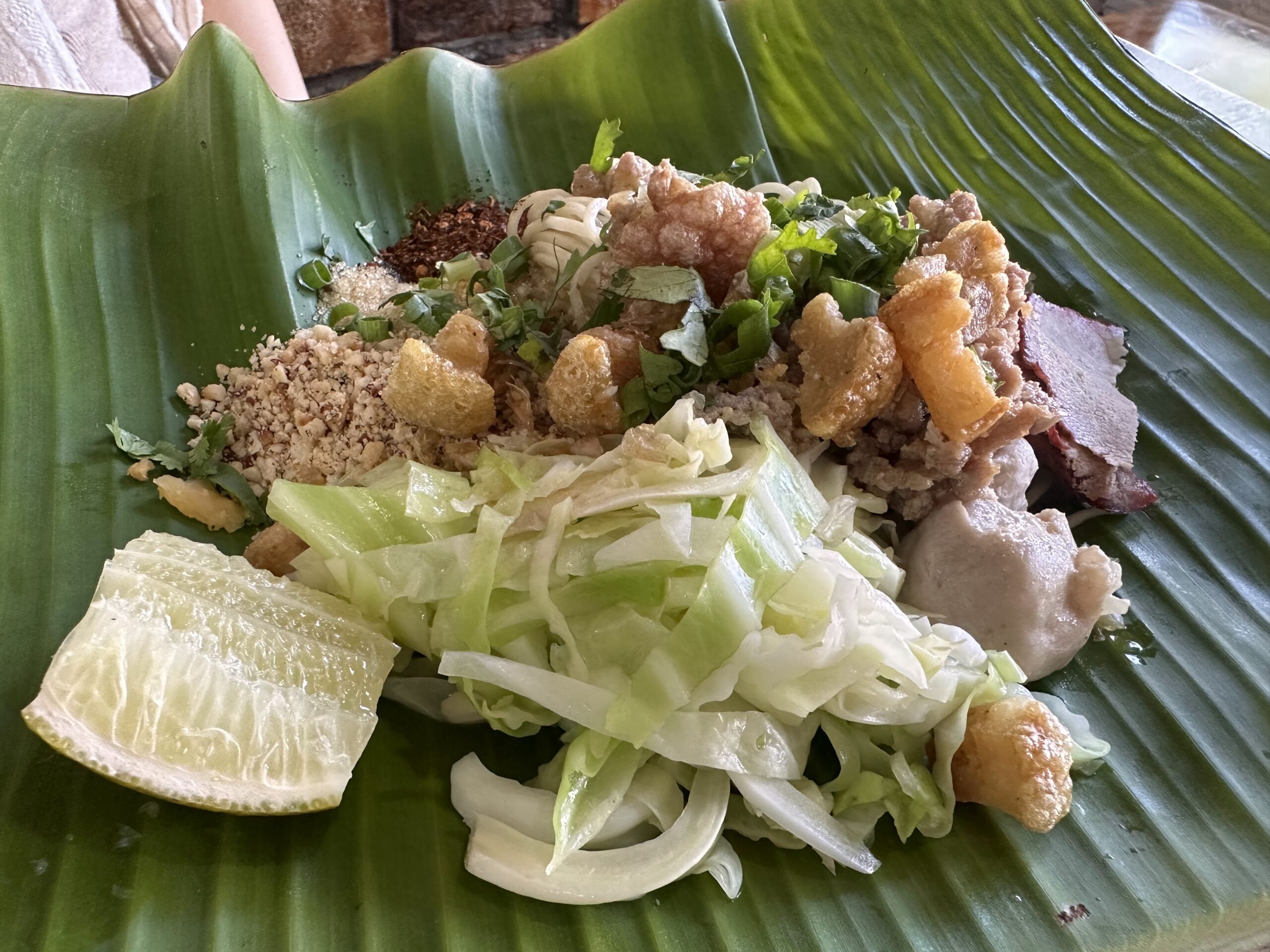 น้ำตกหมูกรอบเสิร์ฟบนใบตองพร้อมผักกาดขาว มะนาว ถั่วคั่ว พริกป่น และผักชี