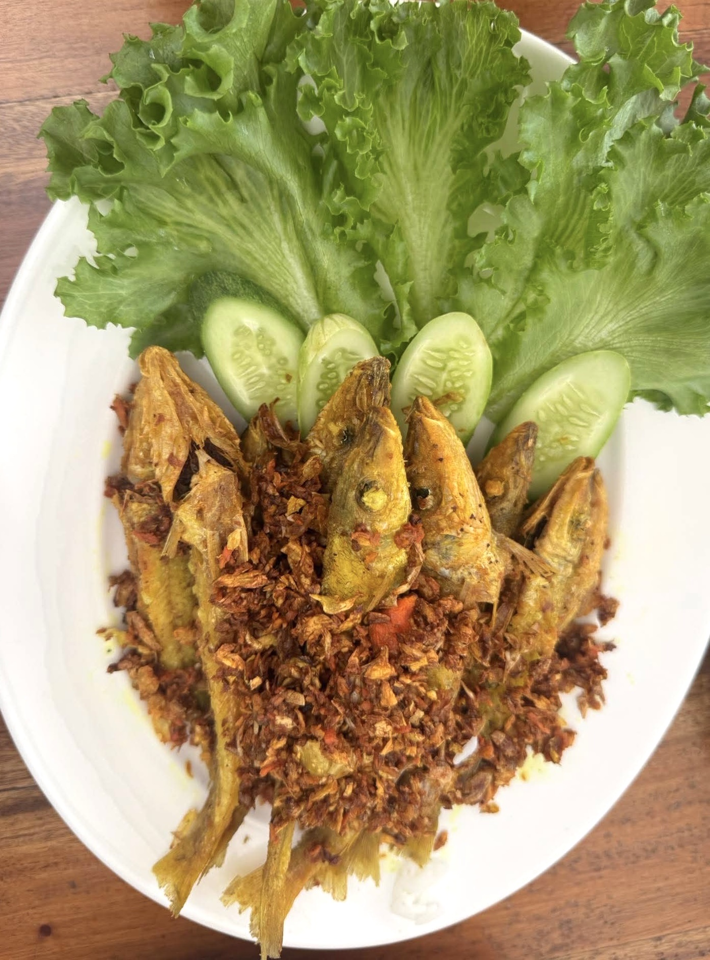 ปลาทอดกระเทียมพริกไทยเสิร์ฟพร้อมผักสลัดและแตงกวาบนจานขาว