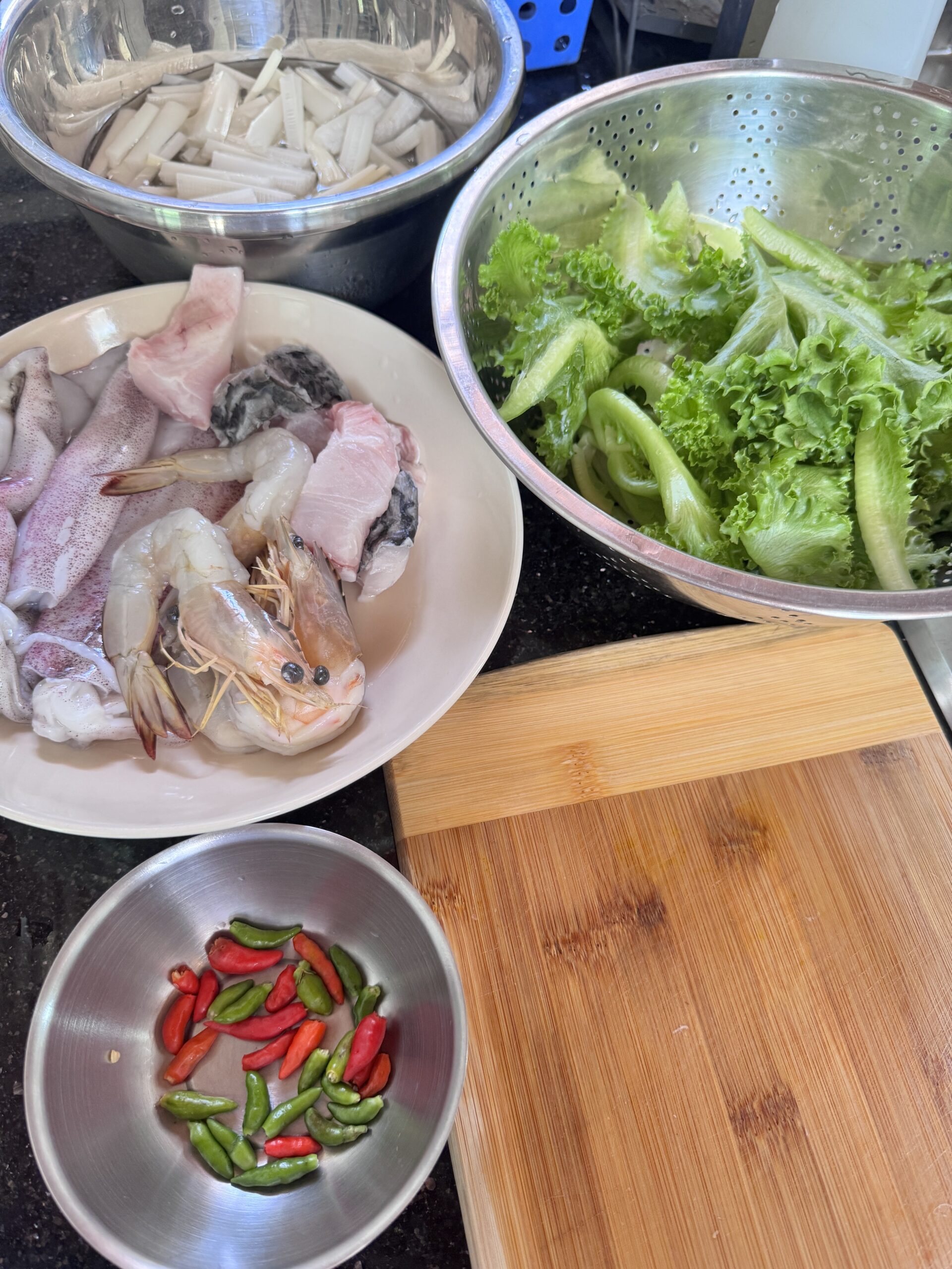 วัตถุดิบสดสำหรับทำอาหาร กุ้ง ปลาหมึก ปลา ผักกาดหอม พริกสด และหัวปลีหั่นบนเคาน์เตอร์ครัว