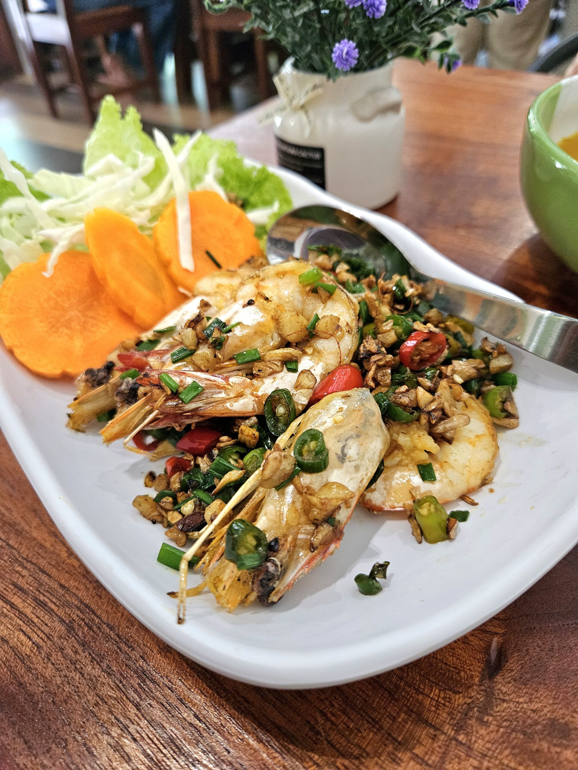 กุ้งทอดกระเทียมพริกไทย โรยด้วยต้นหอมและพริกสด เสิร์ฟพร้อมแครอทและผักสลัดบนจานขาว