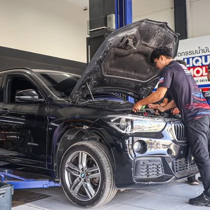 ช่างซ่อมรถยนต์กำลังตรวจเช็คเครื่องยนต์รถ BMW สีดำในอู่ซ่อมรถ
