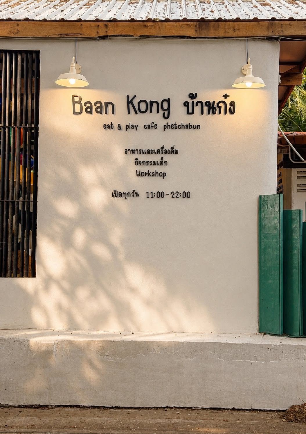 ด้านหน้าร้านบ้านก๋ง คาเฟ่เพชรบูรณ์ ผนังสีขาวพร้อมป้ายชื่อร้าน เปิดทุกวัน 11:00-22:00 มีอาหาร เครื่องดื่ม กิจกรรมเด็ก และ Workshop