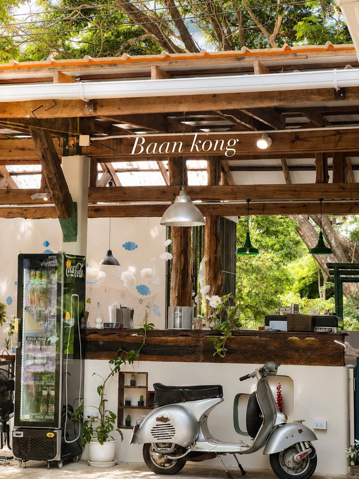 ร้านบ้านก๋ง คาเฟ่สไตล์วินเทจ มีเคาน์เตอร์ไม้เก่า ตู้แช่โค้ก และรถเวสป้าสีเงินจอดหน้าร้าน ท่ามกลางบรรยากาศร่มรื่นใต้ต้นไม้ใหญ่
