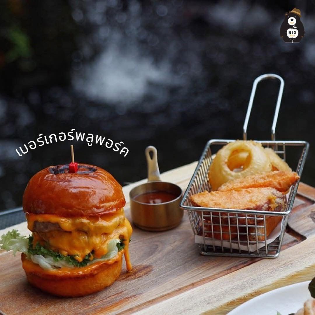 เบอร์เกอร์พูลพอร์คพร้อมชีสเยิ้มบนขนมปังบริออชเสิร์ฟคู่กับออเนียนริงทอดกรอบในตะกร้าเหล็กและซอสบนเขียงไม้