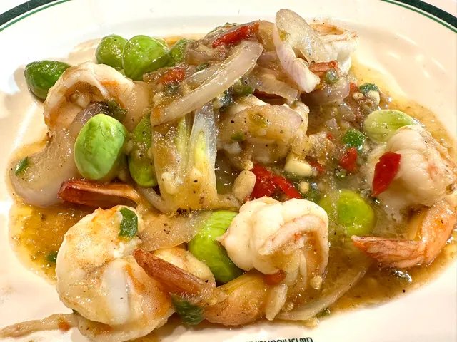 กุ้งผัดสะตอพริกแกง จานอาหารไทยใส่กุ้งตัวโต สะตอเม็ดเขียว หอมแดง และพริกในจานสีขาว