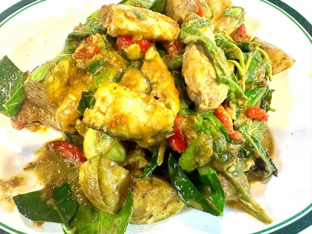 ผัดเขียวหวานไก่กับผักใบเขียวและพริกแดงบนจานขาว