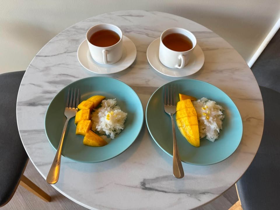 ข้าวเหนียวมะม่วงสองจานบนโต๊ะหินอ่อนพร้อมชาร้อนสองถ้วย