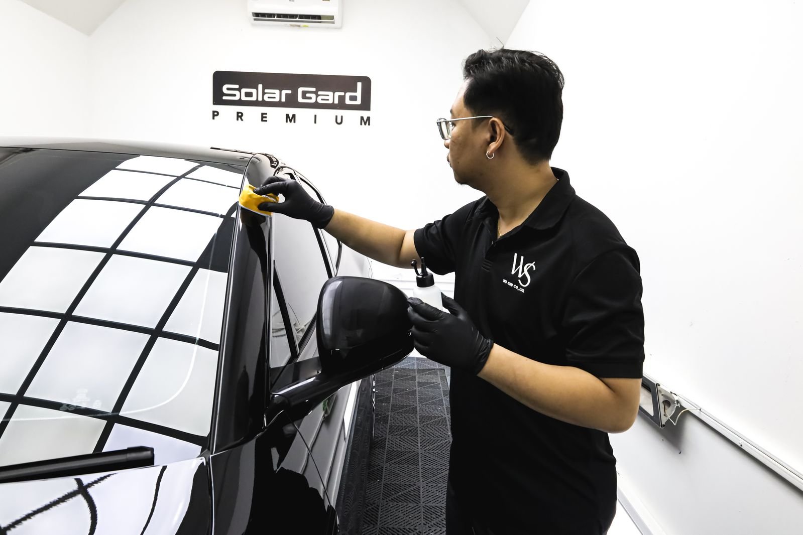 ช่างติดฟิล์มกรองแสง Solar Gard Premium กำลังติดฟิล์มกระจกรถยนต์สีดำในห้องปฏิบัติการสีขาว
